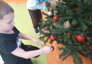 Chłopiec zawiesza bombki na choince