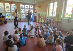 Przedszkolaki słuchają jak Pan Jacek gra na trąbce
