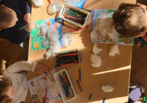 Dzieci kolorują łąkę i naklejają na owce watę jako wełnę